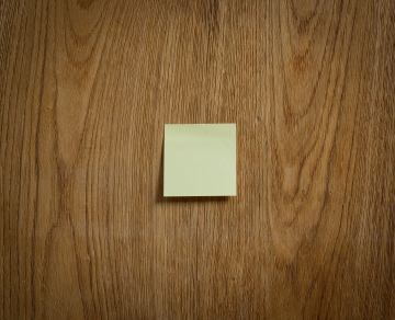 A yellow sticky note stuck to a wooden surface.